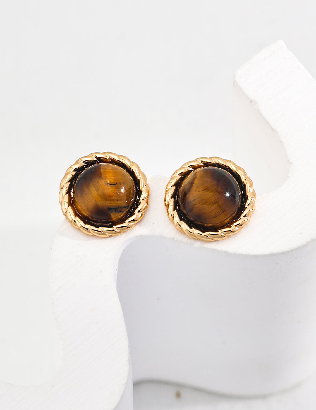 Round Tiger Eye gemstone stud earrings with gold-tone twisted rope bezel on a white abstract display